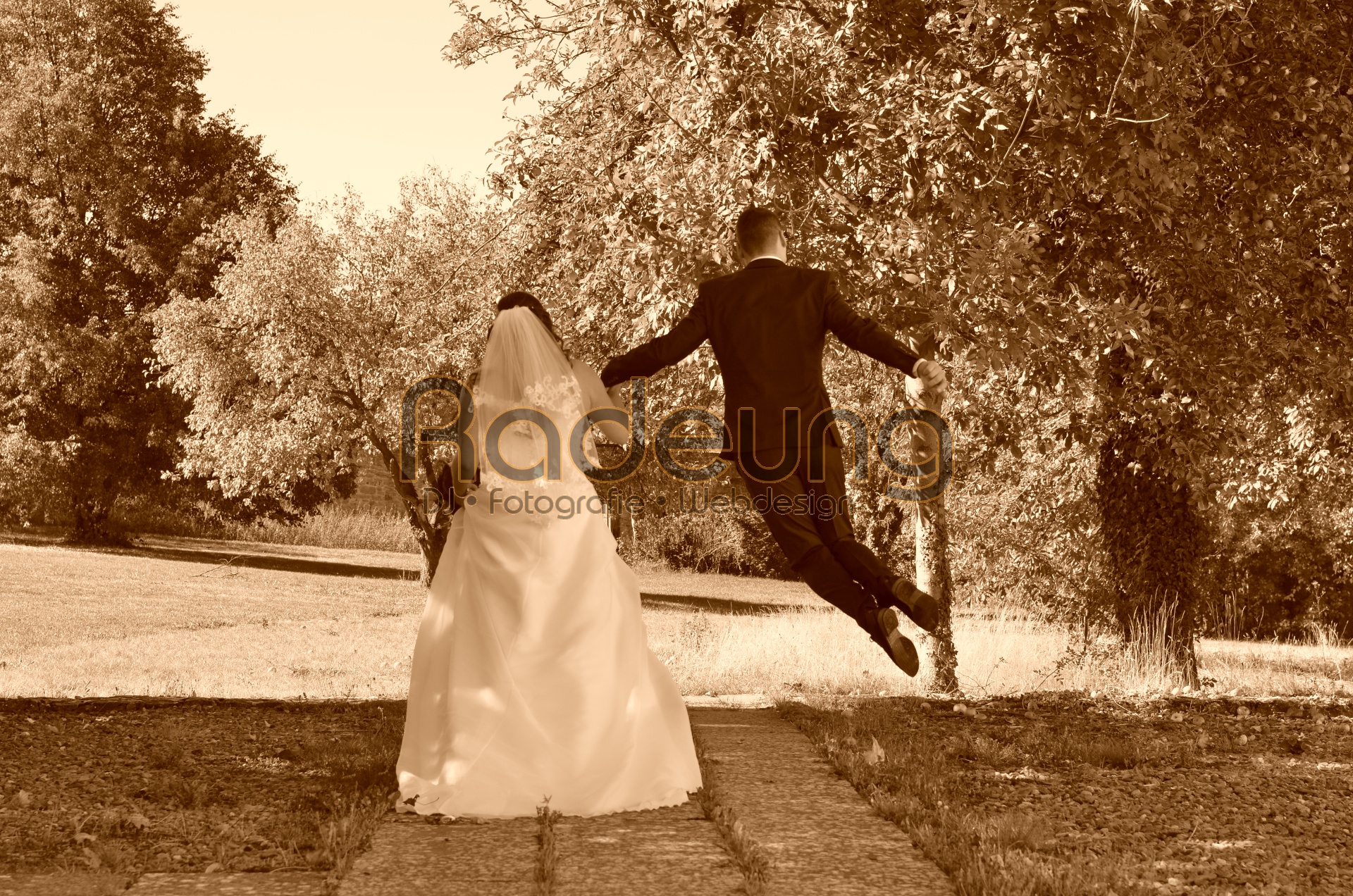 Ein Brautpaar von hinten, der Mann springt vor Freude in die Luft.